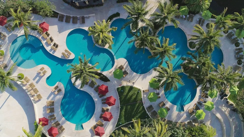 Aerial view of freeform pools at Hacienda Tres Rios Resort, Spa & Nature Park with palms and loungers.