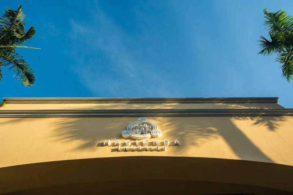 Low-angle view of the Hacienda Tres Rios Resort, Spa & Nature Park facade sign framed by palms.