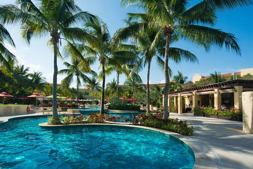 Palm-lined pool courtyard at Hacienda Tres Rios Resort, Spa & Nature Park with loungers and umbrellas.