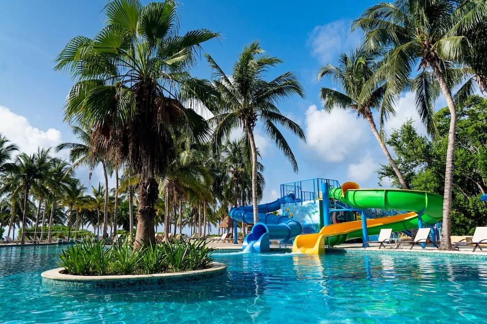 Palm-lined pool with colorful waterslides at Hacienda Tres Rios Resort, Spa & Nature Park.