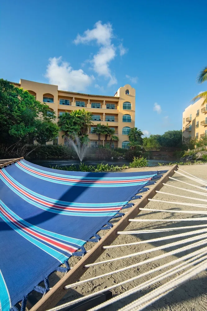 Striped hammock by the lagoon at Hacienda Tres Rios Resort, Spa & Nature Park with buildings behind.