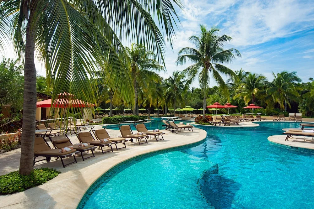 Sunny resort pool at Hacienda Tres Rios Resort, Spa & Nature Park with loungers, palms, and umbrellas.