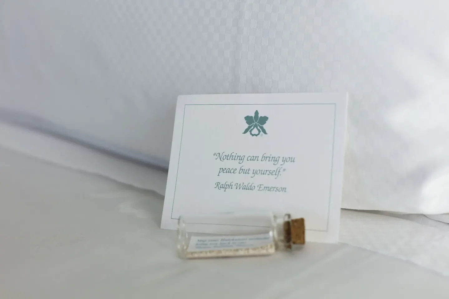 Bedside welcome card and small glass vial on white linens at Halekulani.