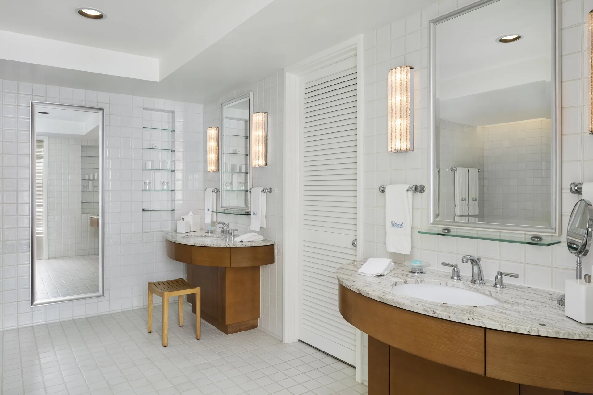 Bathroom with two vanities, mirrors, white tile, and louvered door at Halekulani.