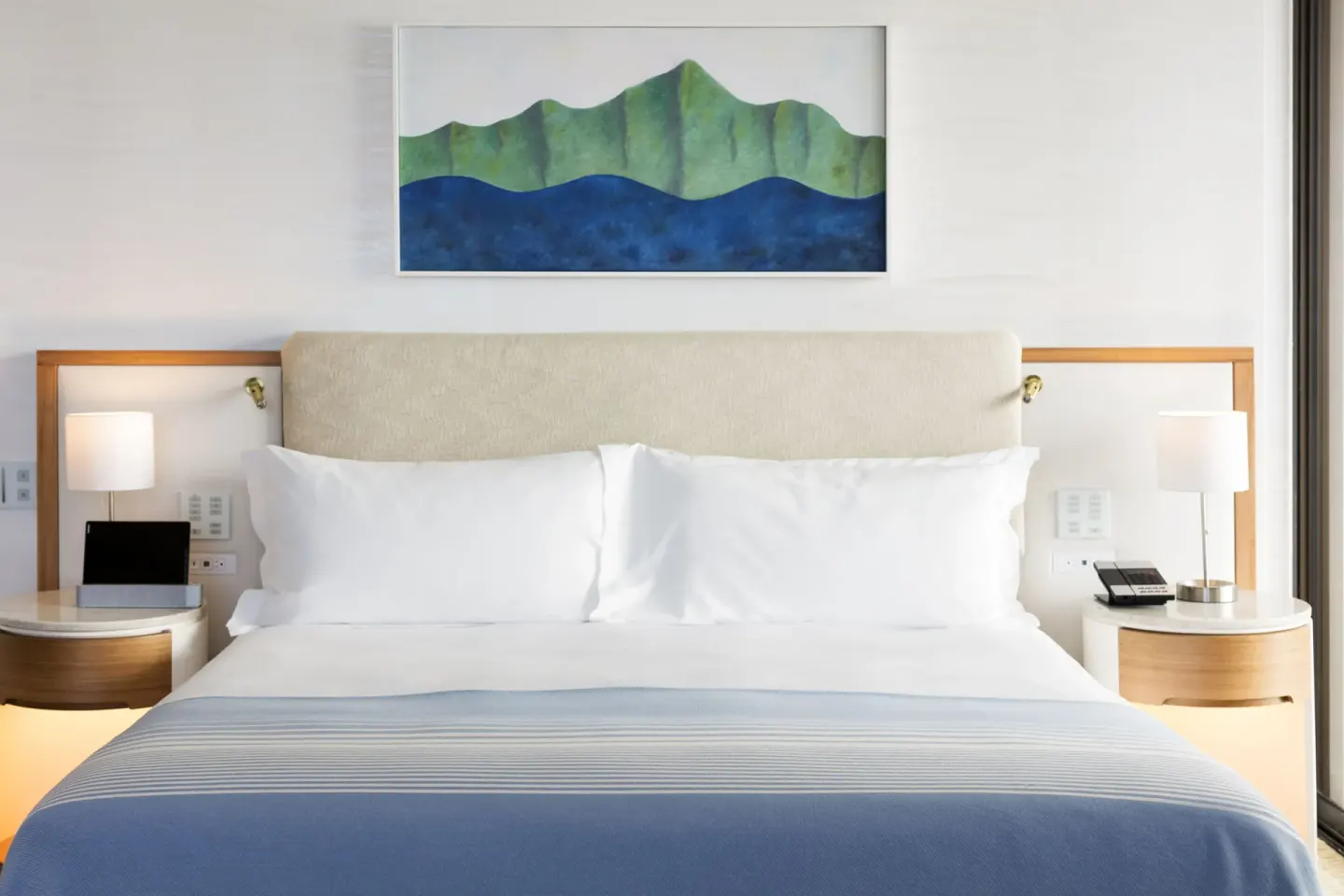 King bed with blue throw, bedside lamps, and mountain artwork at Halekulani.