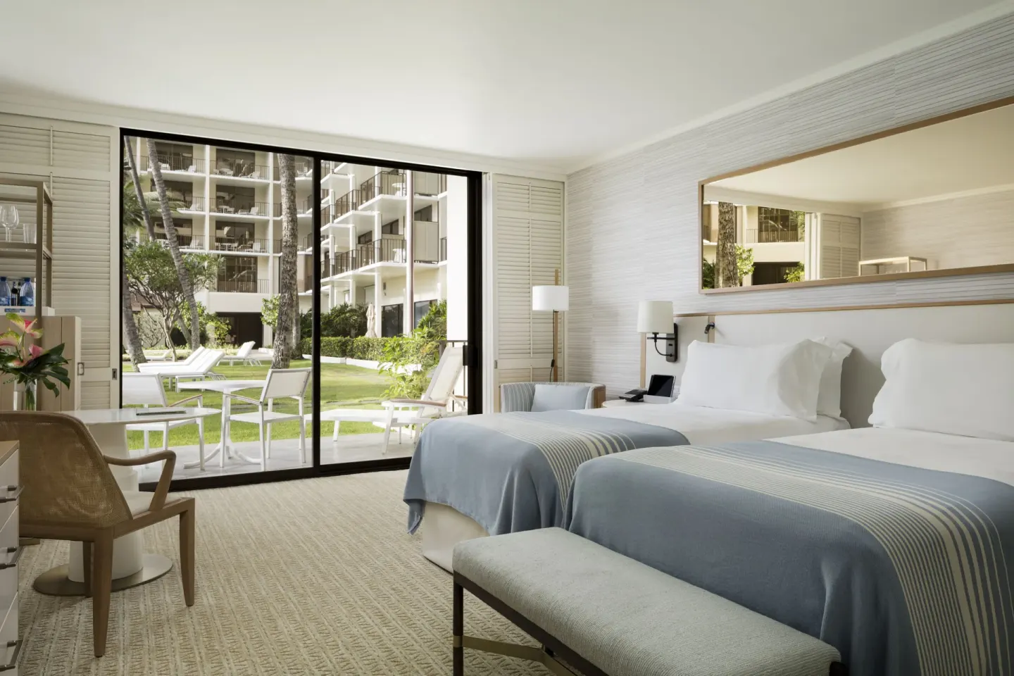 Two-bed guest room at Halekulani with sliding doors opening to lawn and lounge chairs.