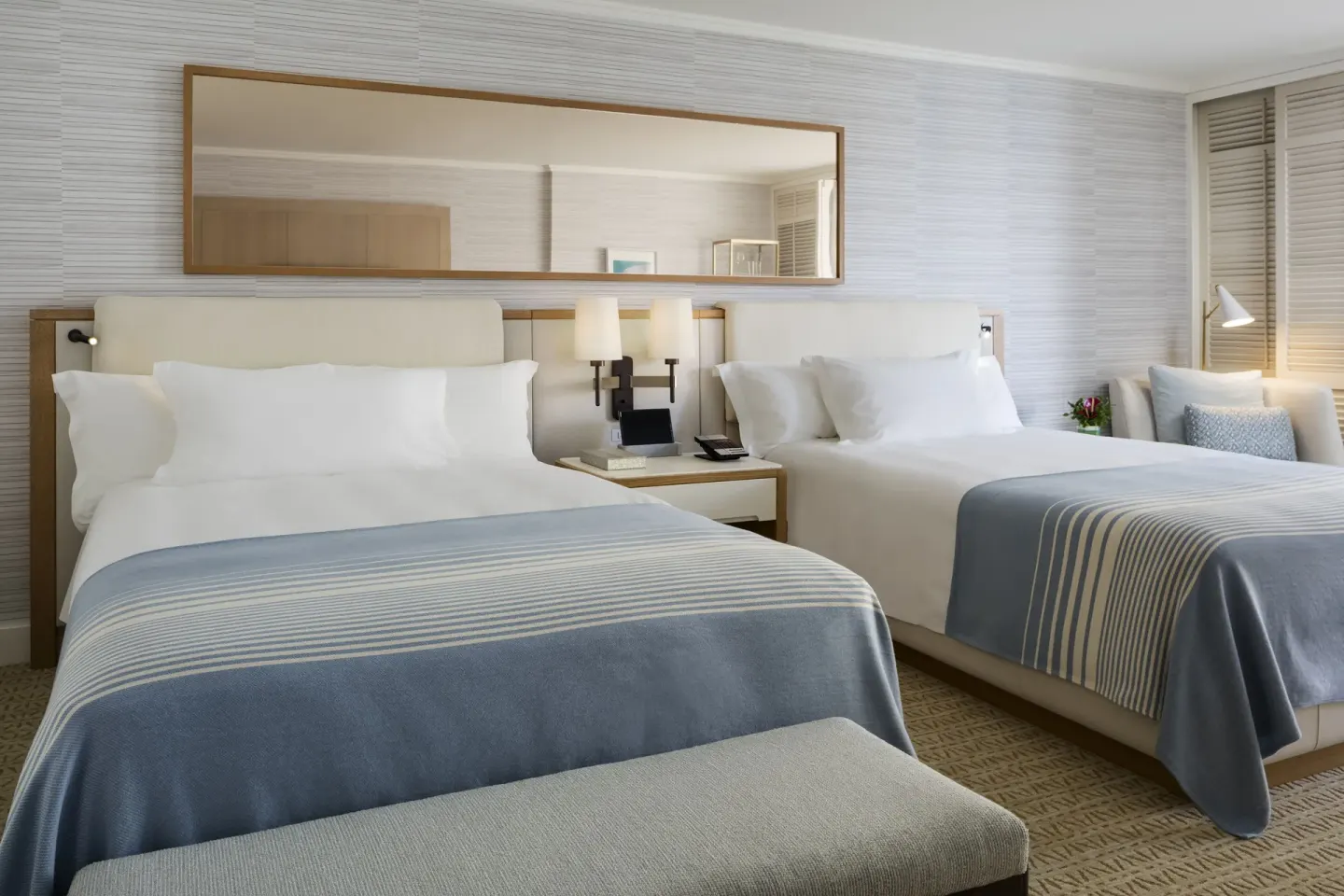 Two-bed guest room at Halekulani with a long wall mirror and bedside seating.