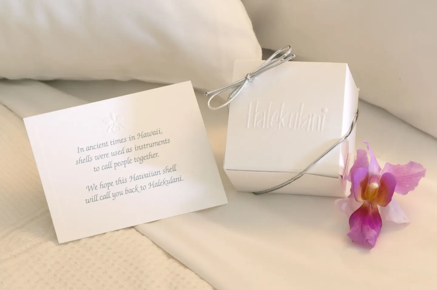 Halekulani keepsake box, note card, and orchid set on a bed.