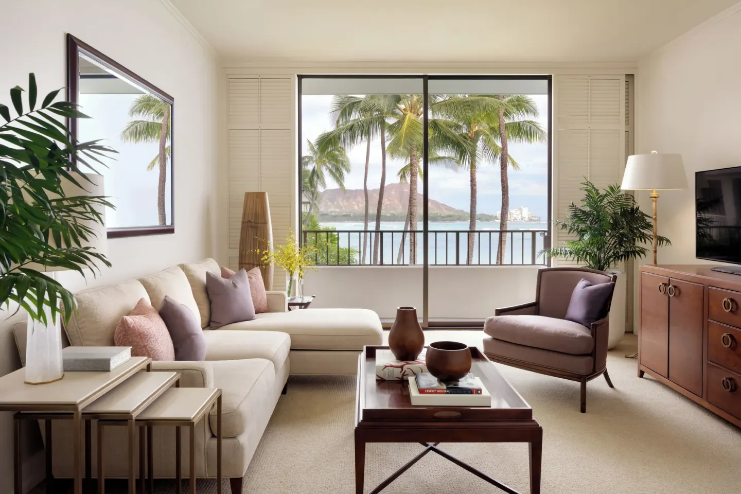 Living room with sofa, armchair, and balcony view of palms and Diamond Head at Halekulani.