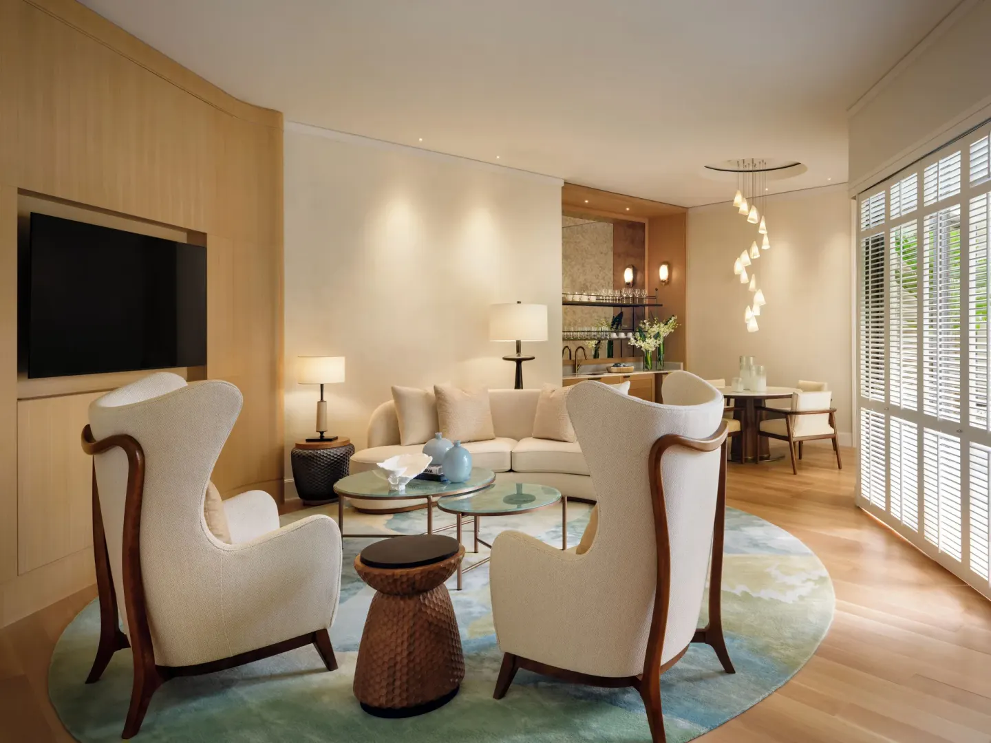 Living room with curved sofa, lounge chairs, dining area, and shuttered windows at Halekulani.