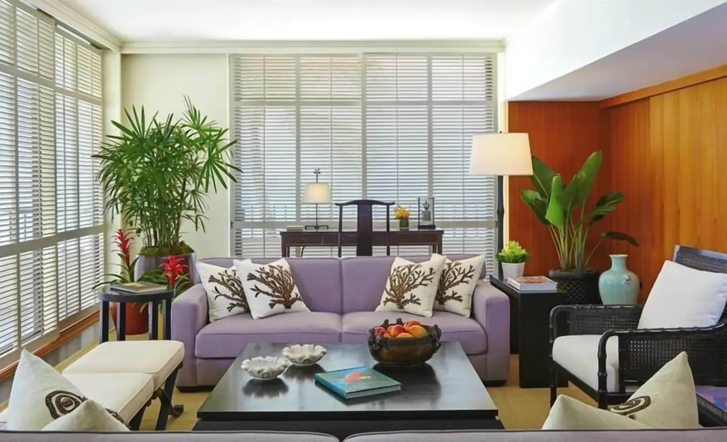 Living room with lavender sofa, tropical plants, wood wall, and shuttered windows at Halekulani.