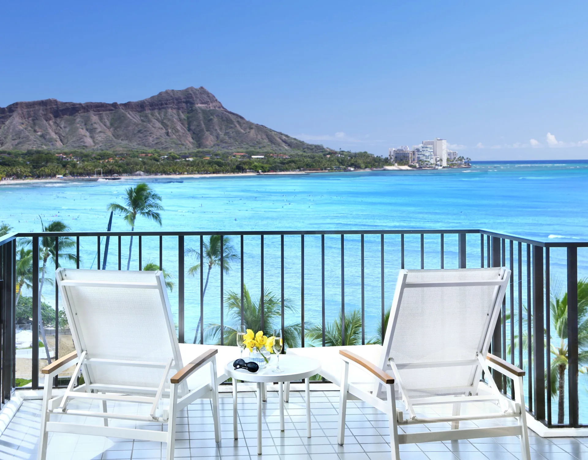 Halekulani balcony with two lounge chairs overlooking turquoise water and Diamond Head.