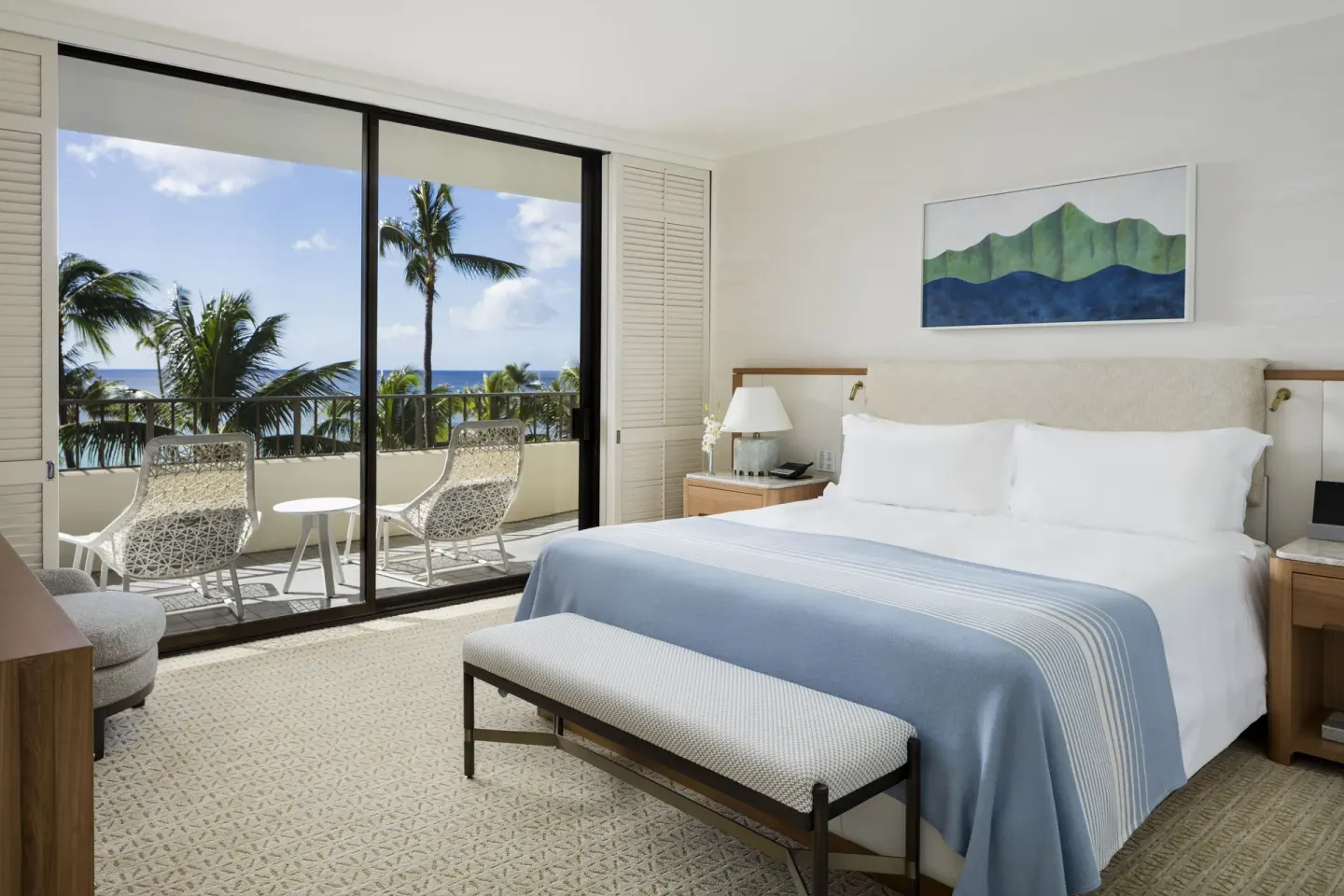 Ocean-view guest room with king bed, bench, and balcony chairs at Halekulani.