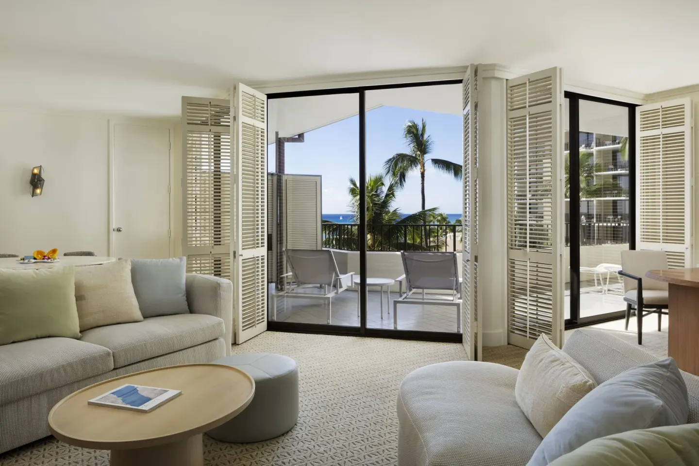 Suite living room with sofas and balcony lounge chairs facing the ocean at Halekulani.