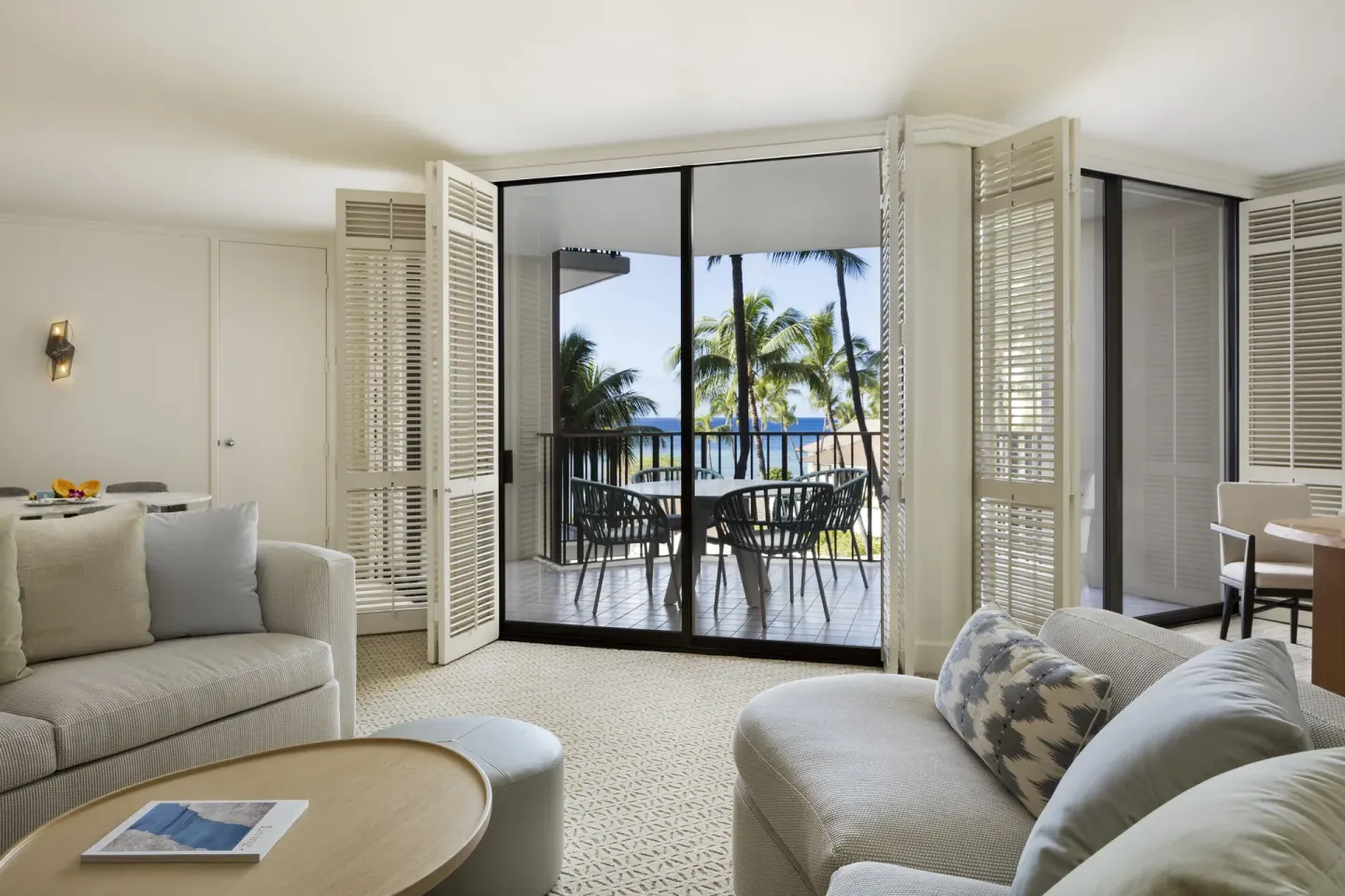 Living room seating opens to a balcony with palm and ocean views at Halekulani.