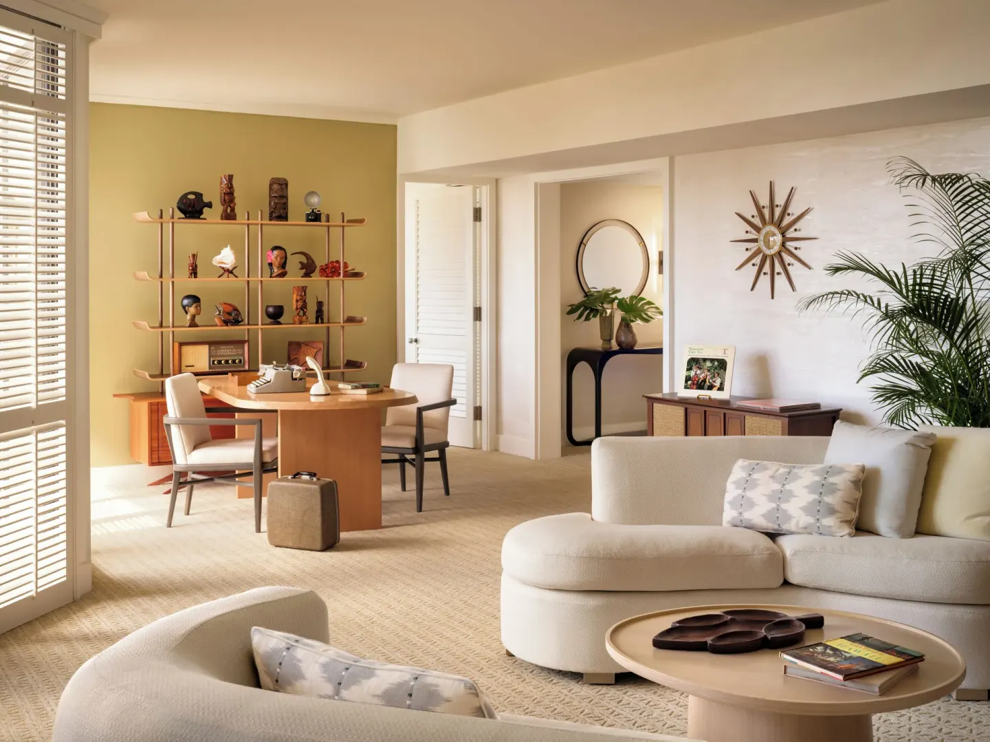 Suite living room with sofa, desk, display shelves, and tropical accents at Halekulani.