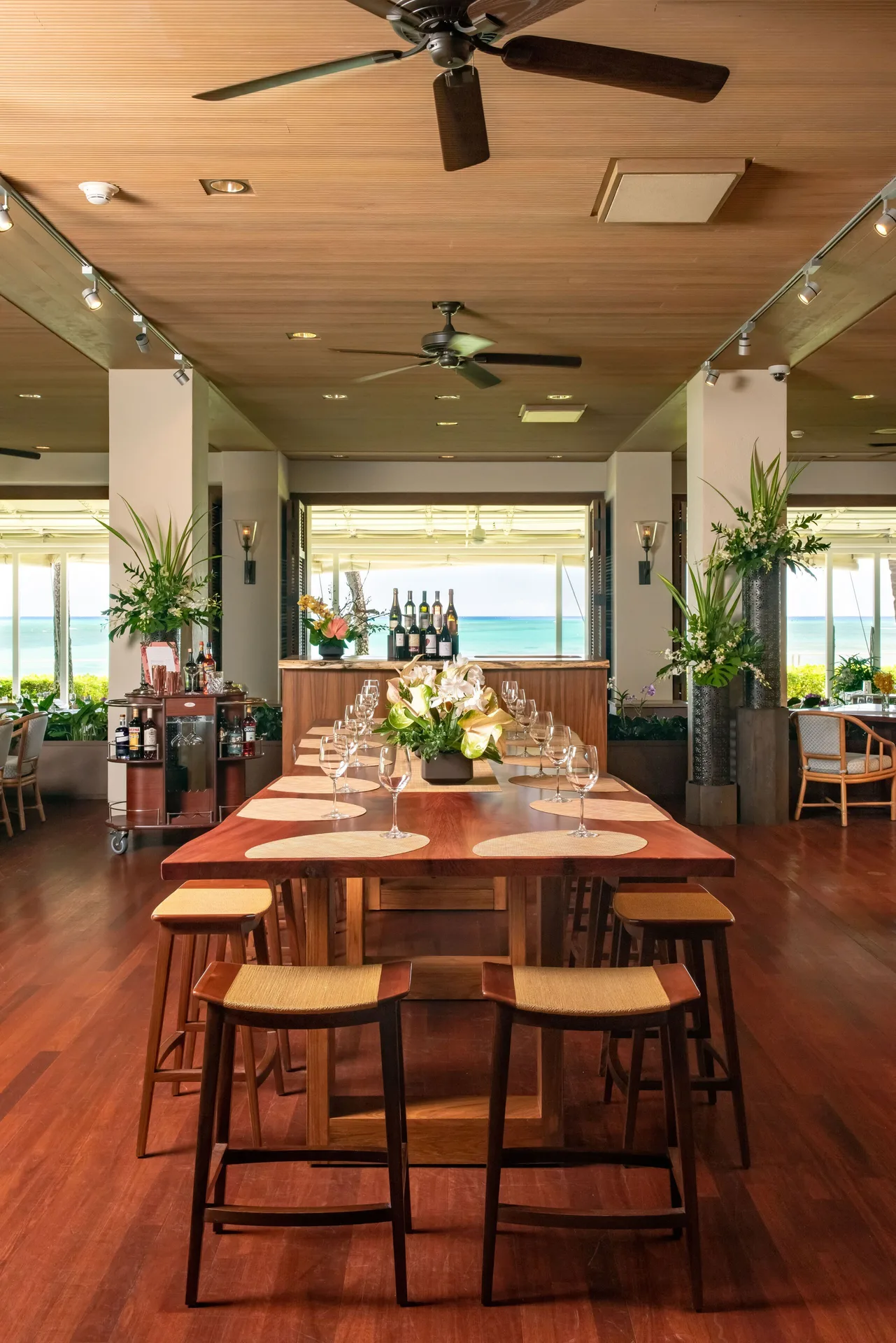 A communal tasting table is set with wine glasses and flowers inside Halekulani.