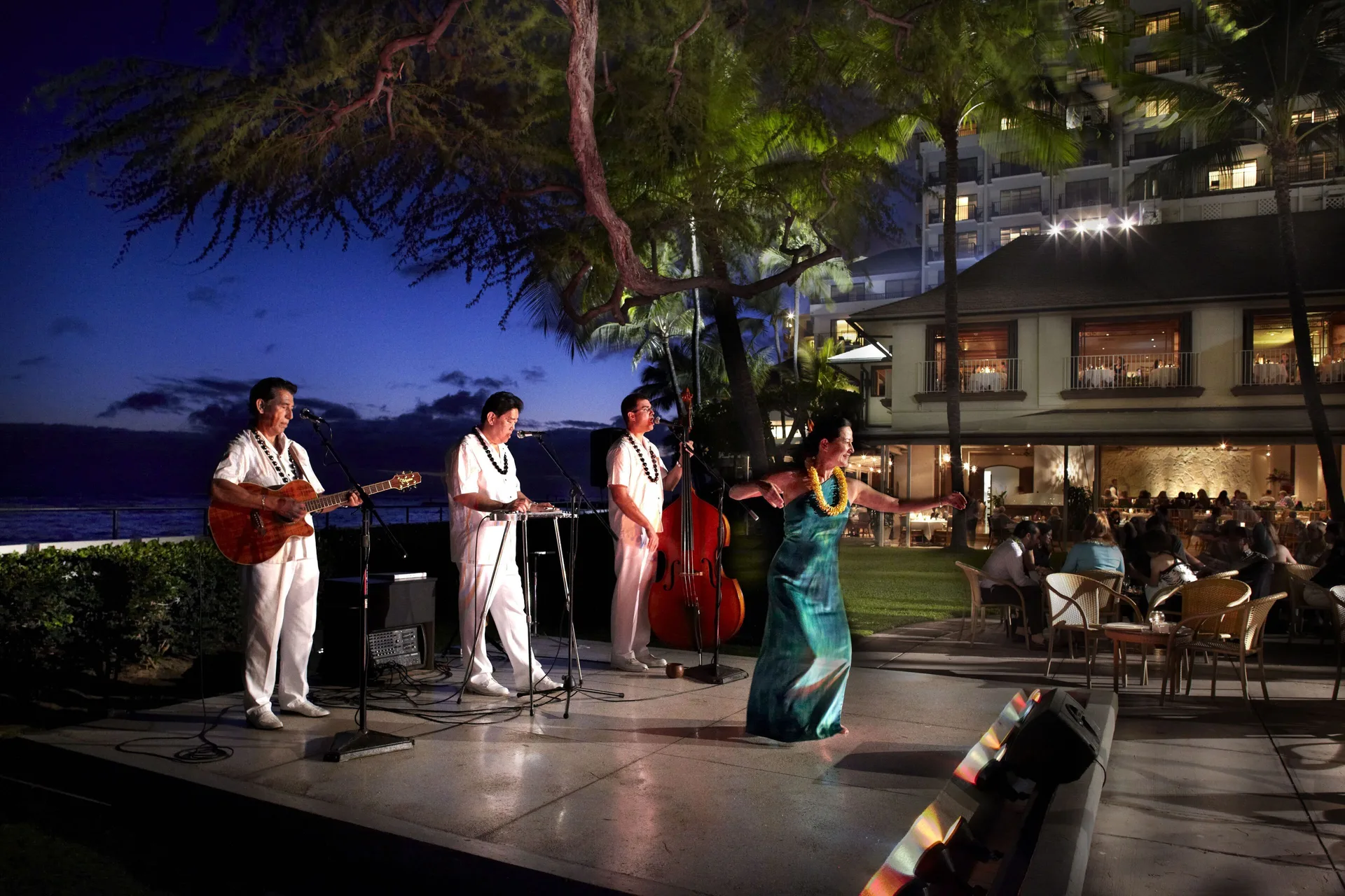 Musicians and a hula dancer perform outdoors at night at Halekulani.