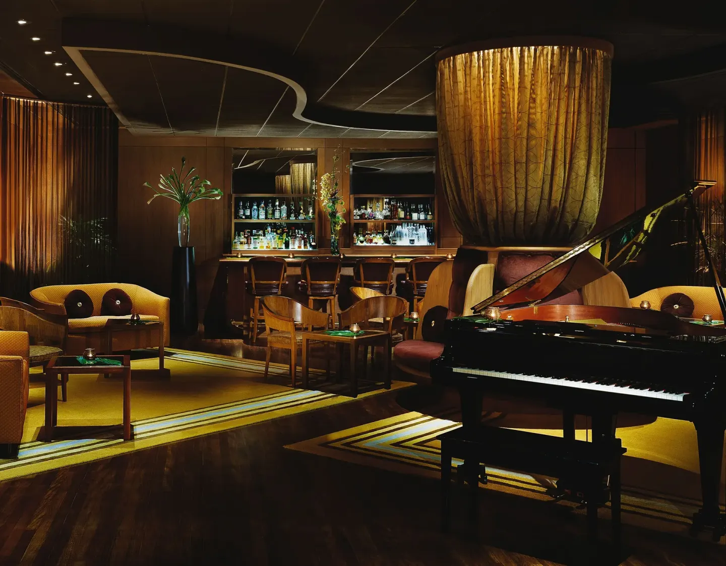 A grand piano sits beside lounge seating and a backlit bar at Halekulani.