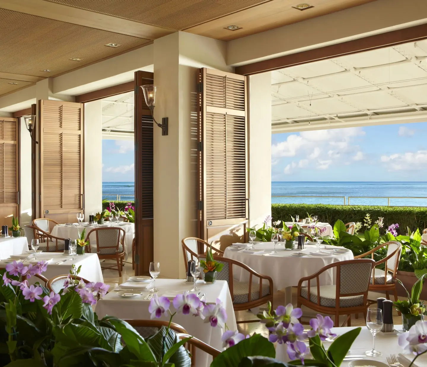 Oceanfront dining room with white tablecloths and orchids at Halekulani.