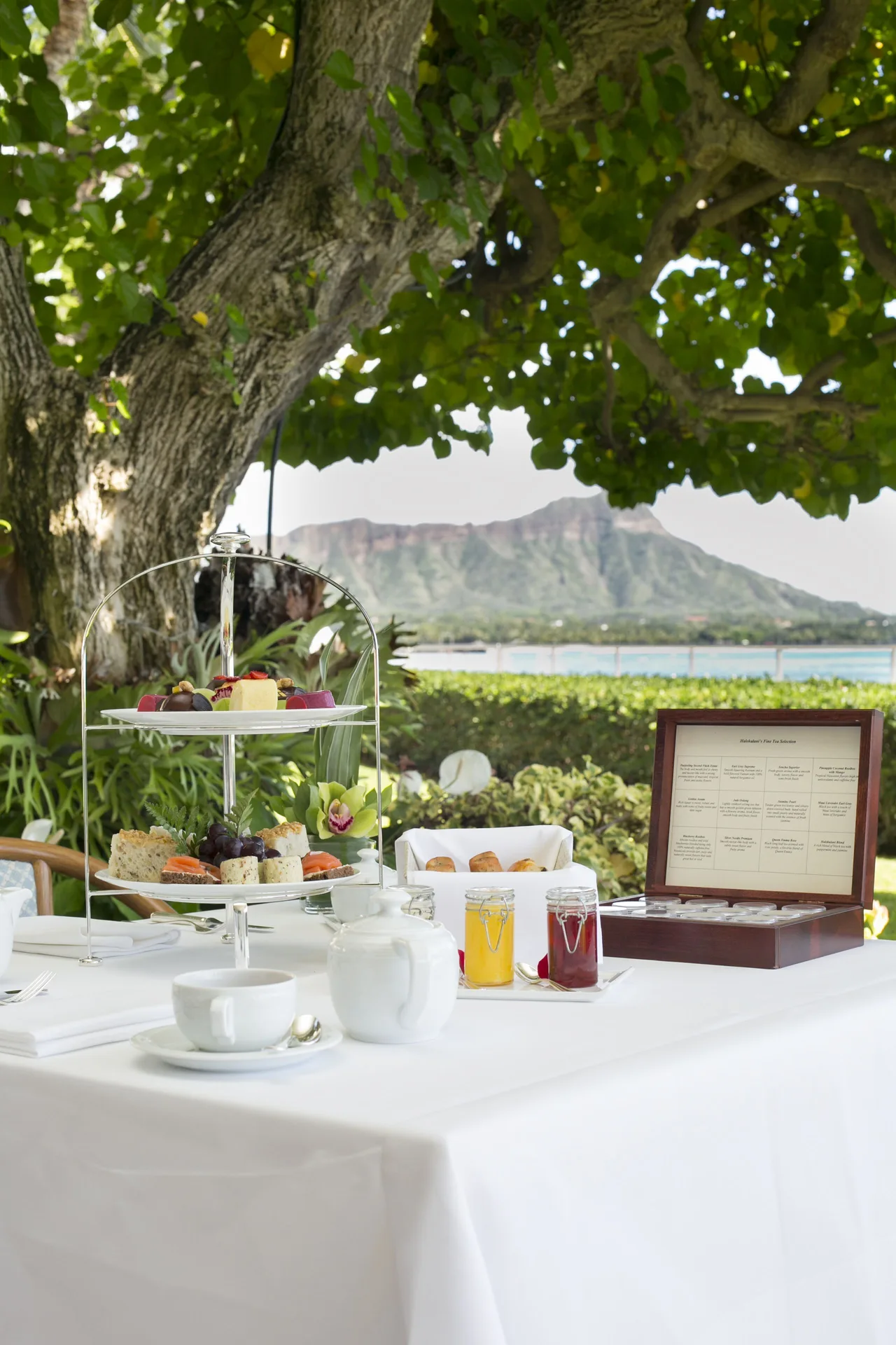 Afternoon tea service under a tree with Diamond Head beyond Halekulani.