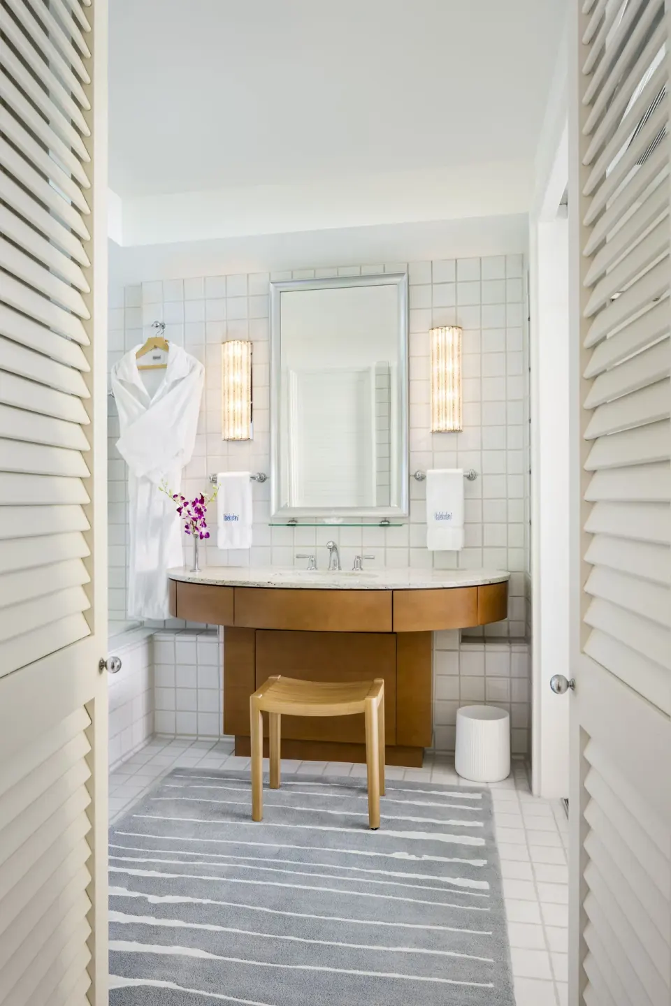 Guest room bathroom vanity with robe, mirror, and louvered doors at Halekulani.