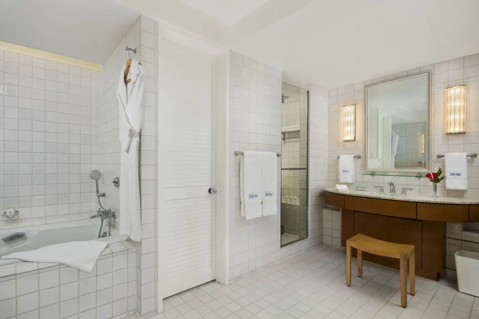 Poolside Suite bathroom with tiled soaking tub, vanity, robes, and mirrors at Halekulani.