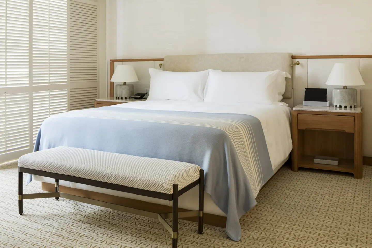 Poolside Suite bedroom with king bed, bench, lamps, and shutters at Halekulani.