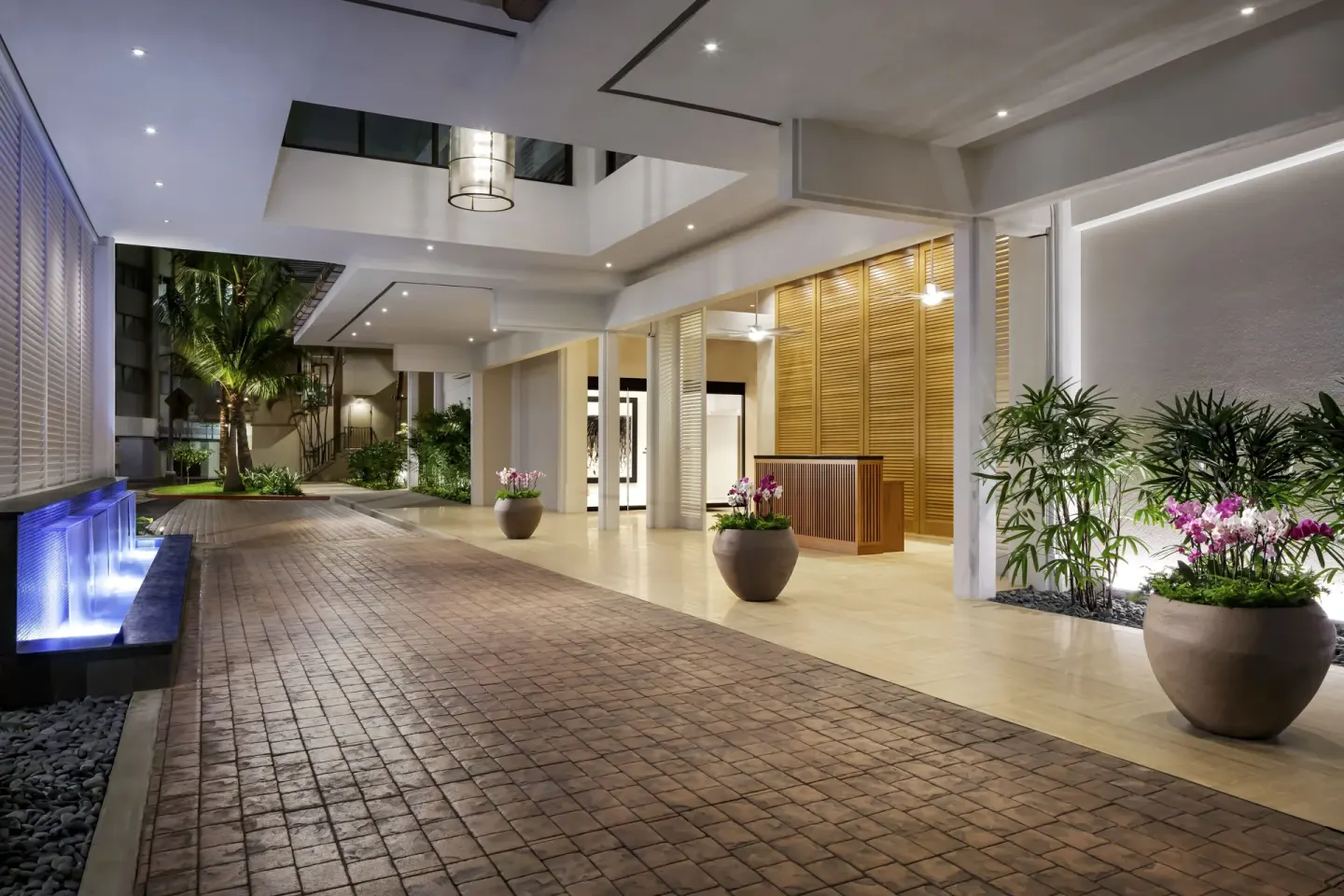 Covered resort entry walkway with planters and blue-lit water feature at Halepuna Waikiki by Halekulani.