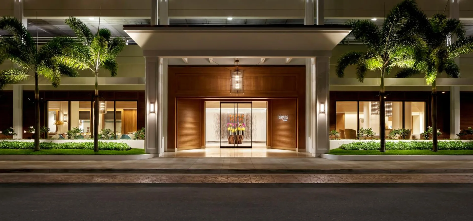Illuminated front entrance and palms at Halepuna Waikiki by Halekulani.