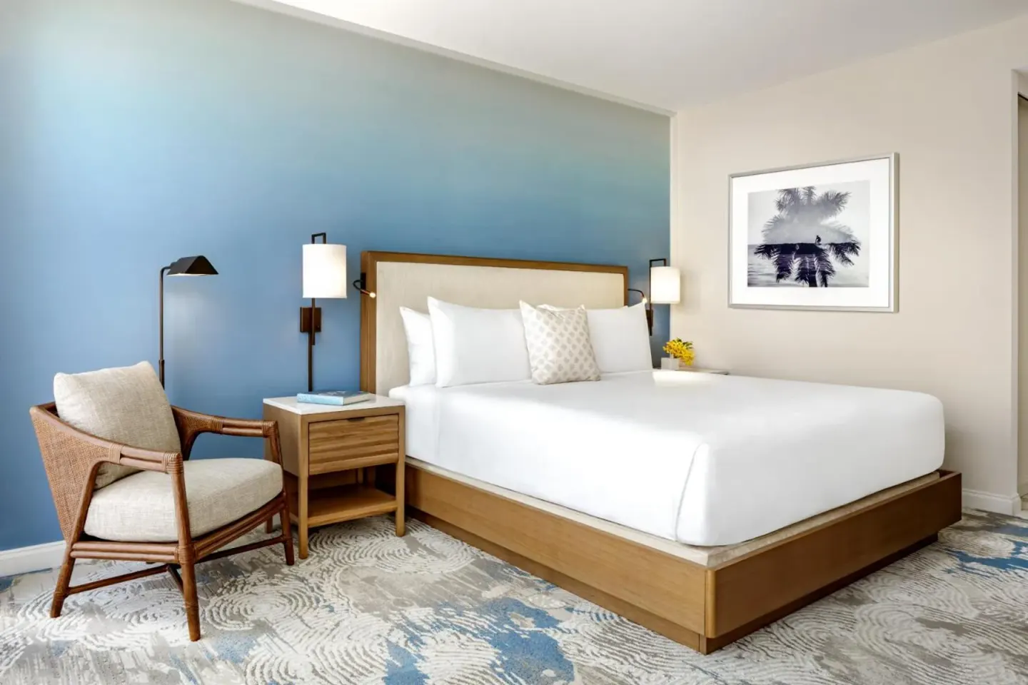 Guest room with a king bed, blue accent wall, and lounge chair at Halepuna Waikiki by Halekulani.