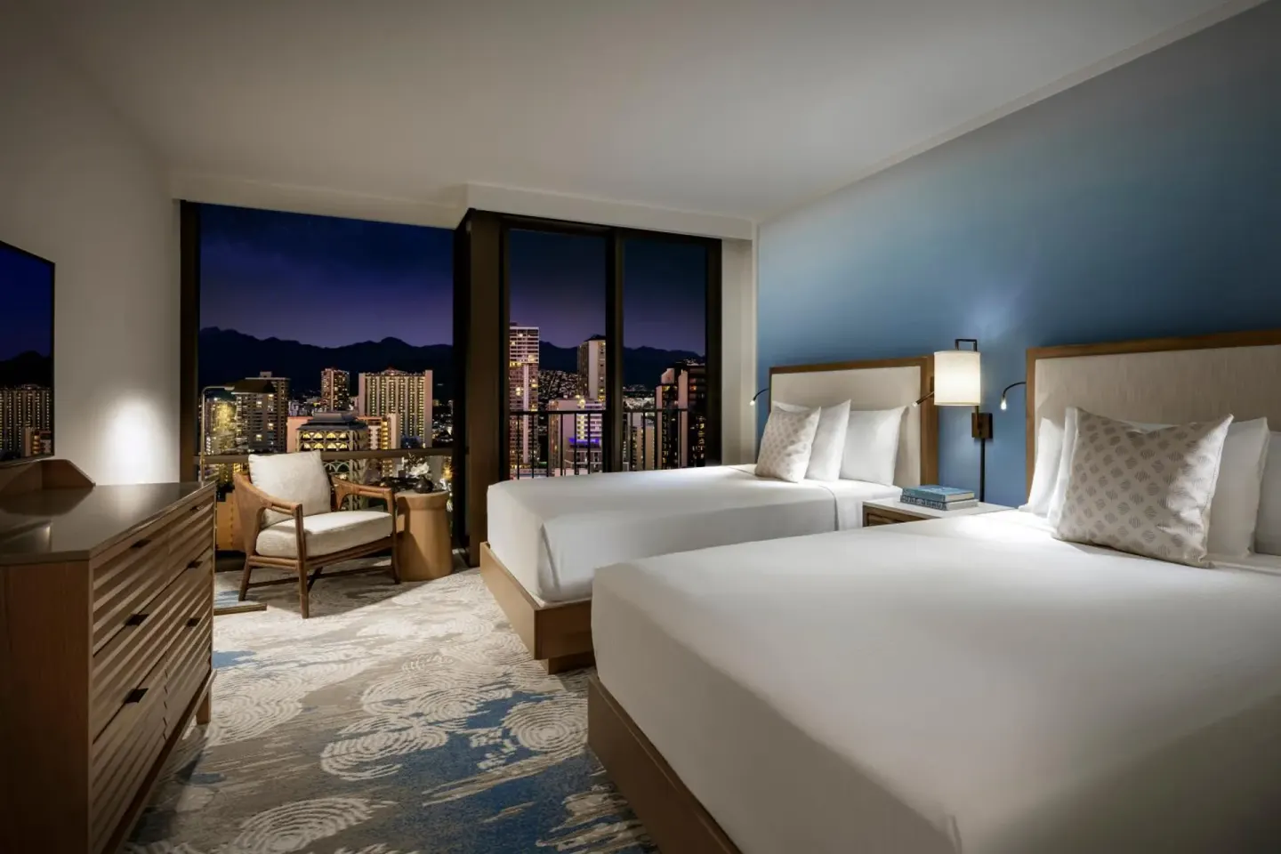 Guest room with two beds and nighttime city views at Halepuna Waikiki by Halekulani.