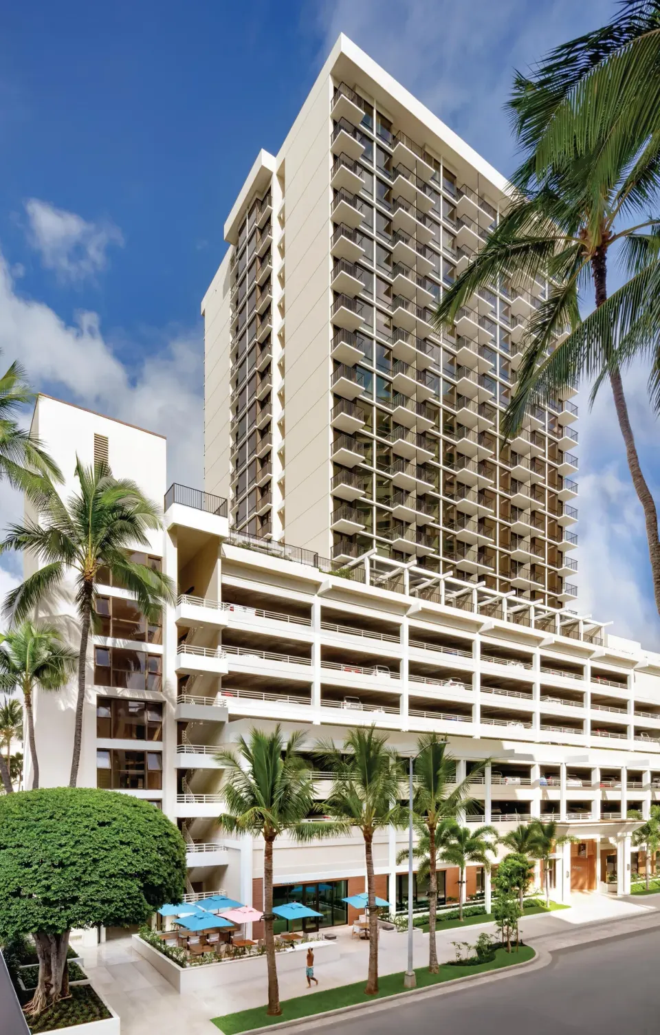 Tall hotel tower with balconies and palm trees at Halepuna Waikiki by Halekulani.
