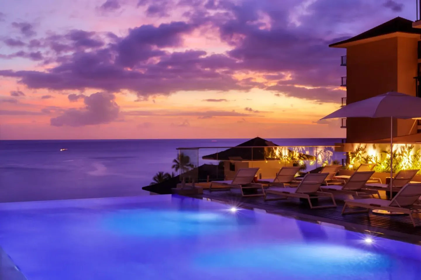 Infinity pool and lounge chairs at sunset at Halepuna Waikiki by Halekulani.