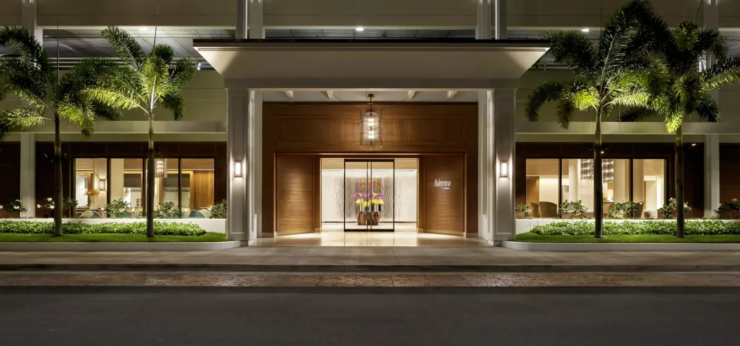 Nighttime hotel entrance with palms and a lit doorway at Halepuna Waikiki by Halekulani.
