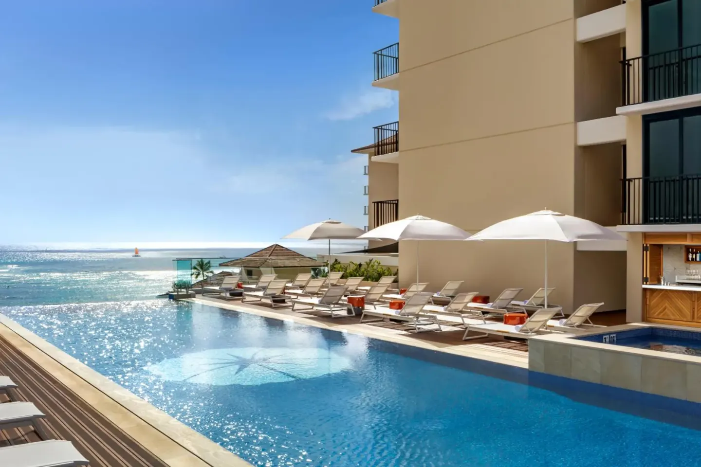 Sunny pool deck with loungers, umbrellas, and ocean view at Halepuna Waikiki by Halekulani.