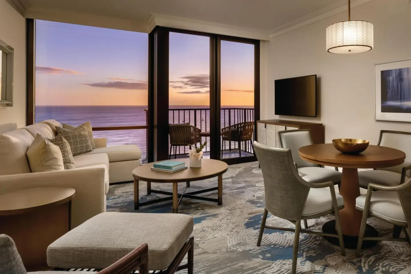Suite living area with oceanfront balcony at sunset at Halepuna Waikiki by Halekulani.