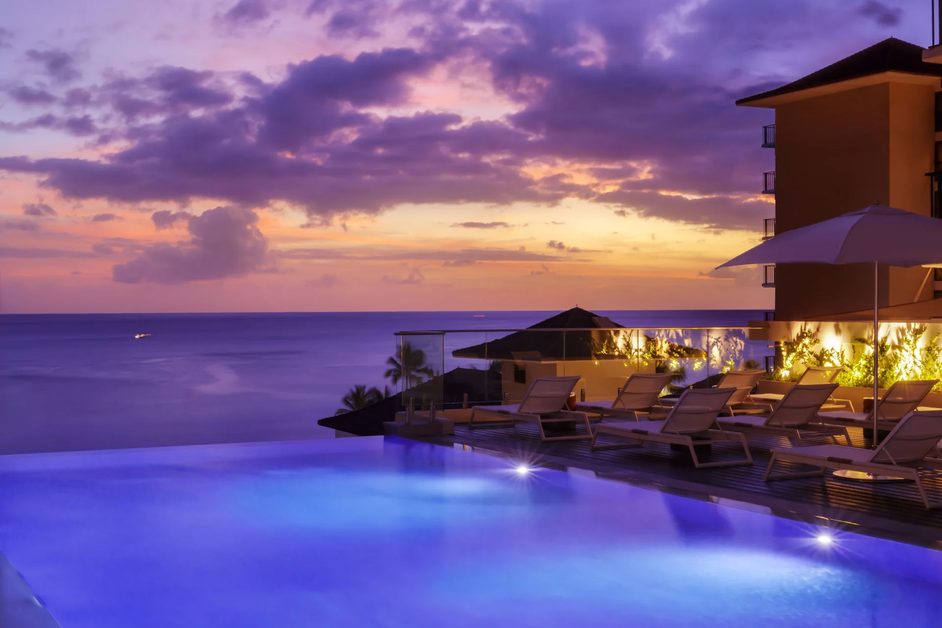 Infinity-style pool glowing at sunset over the ocean at Halepuna Waikiki by Halekulani.