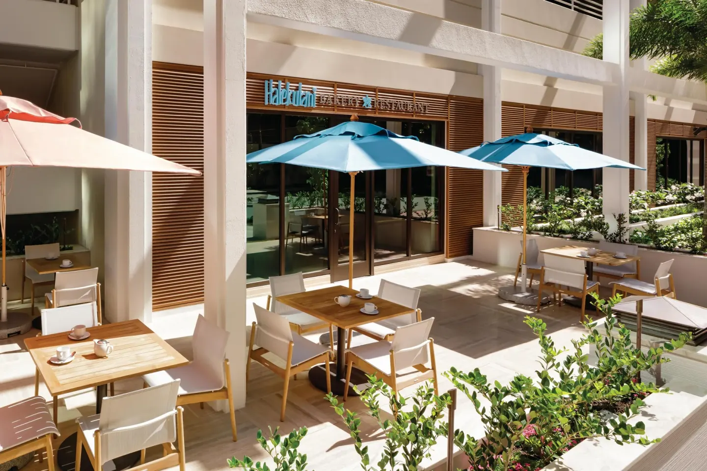 Outdoor café tables and umbrellas outside Halekulani Bakery at Halepuna Waikiki by Halekulani.