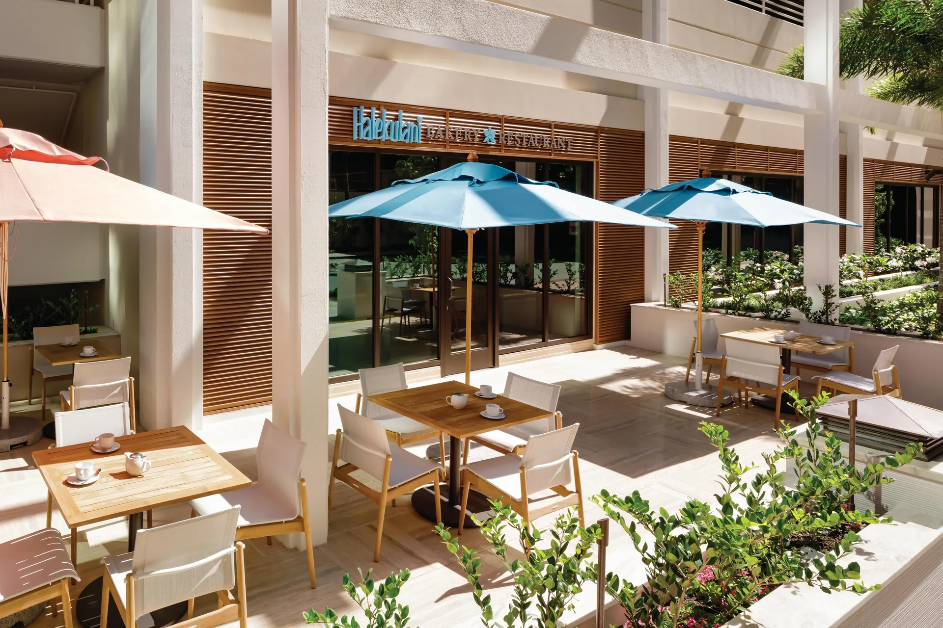 Outdoor café tables and umbrellas outside Halekulani Bakery at Halepuna Waikiki by Halekulani.