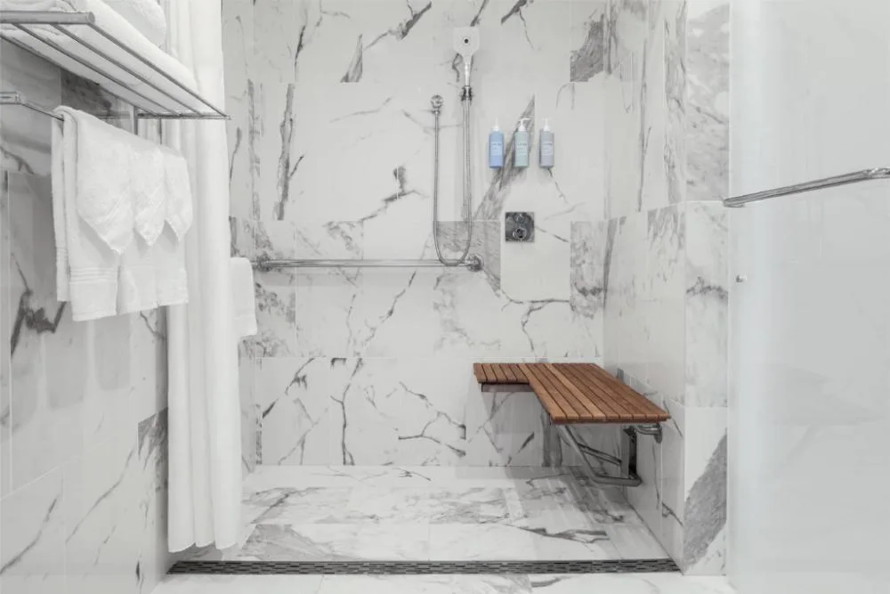 Accessible marble-style roll-in shower with bench in Ocean View One Accessible Bed at Halepuna Waikiki by Halekulani.