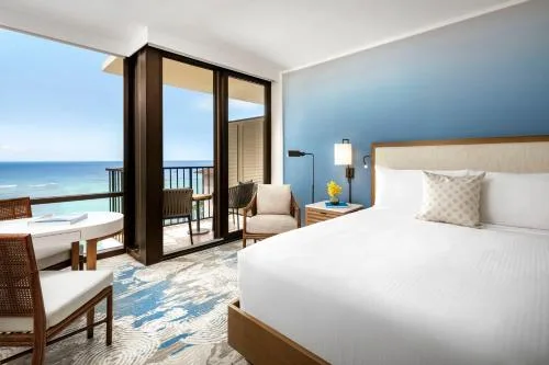 Ocean-facing guest room with bed, chair, and balcony seating at Halepuna Waikiki by Halekulani.
