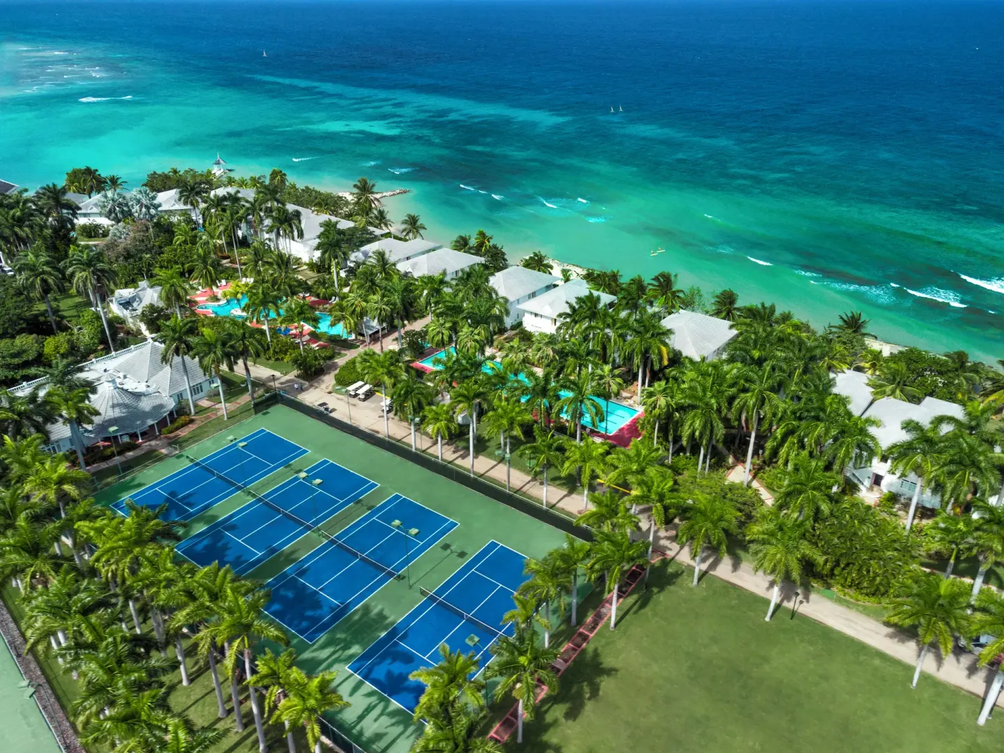 Aerial view of tennis courts, palms, pools, and turquoise shoreline at Half Moon.