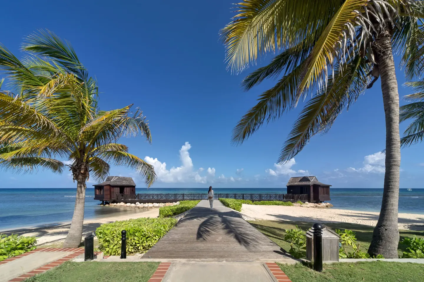 A boardwalk leads between palms to overwater huts and the beach at Half Moon.