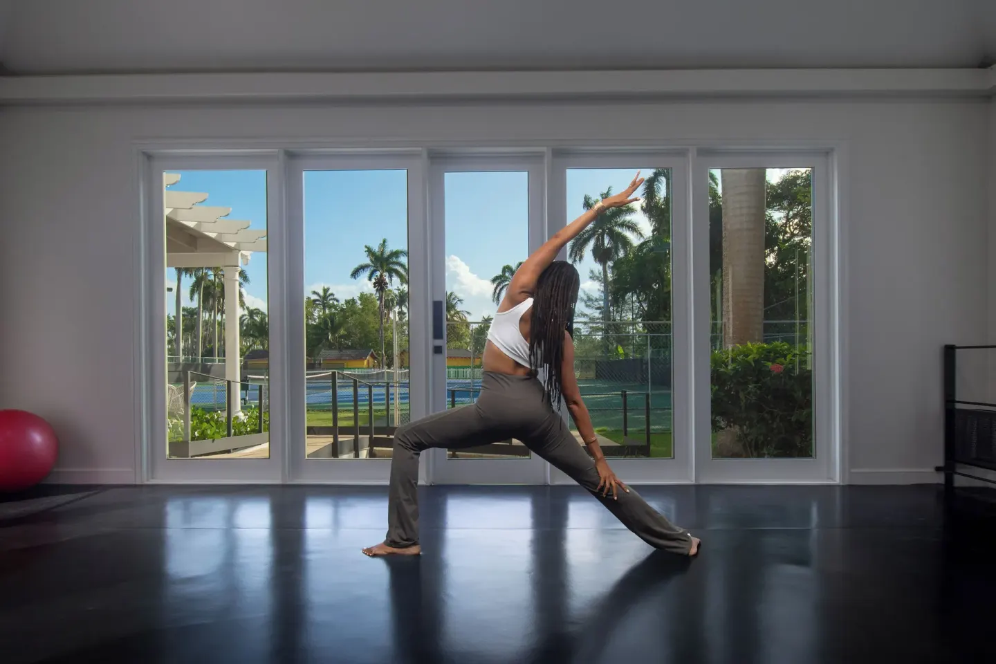 A person stretches in a bright fitness studio at Half Moon with tennis courts outside.