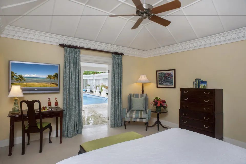 Guest room at Half Moon with a white bed, desk, armchair, dresser, and doorway to a pool terrace.