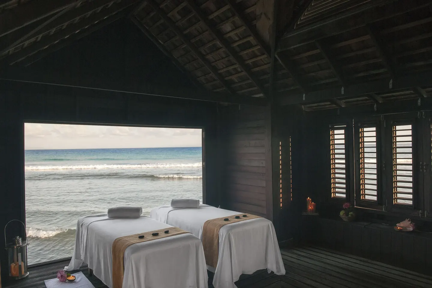 Two spa treatment beds face a wide ocean window in a wooden room at Half Moon.