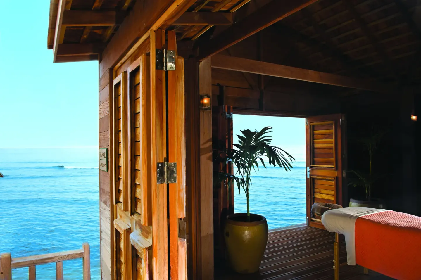 An oceanfront wooden spa room with an open doorway and treatment bed at Half Moon.