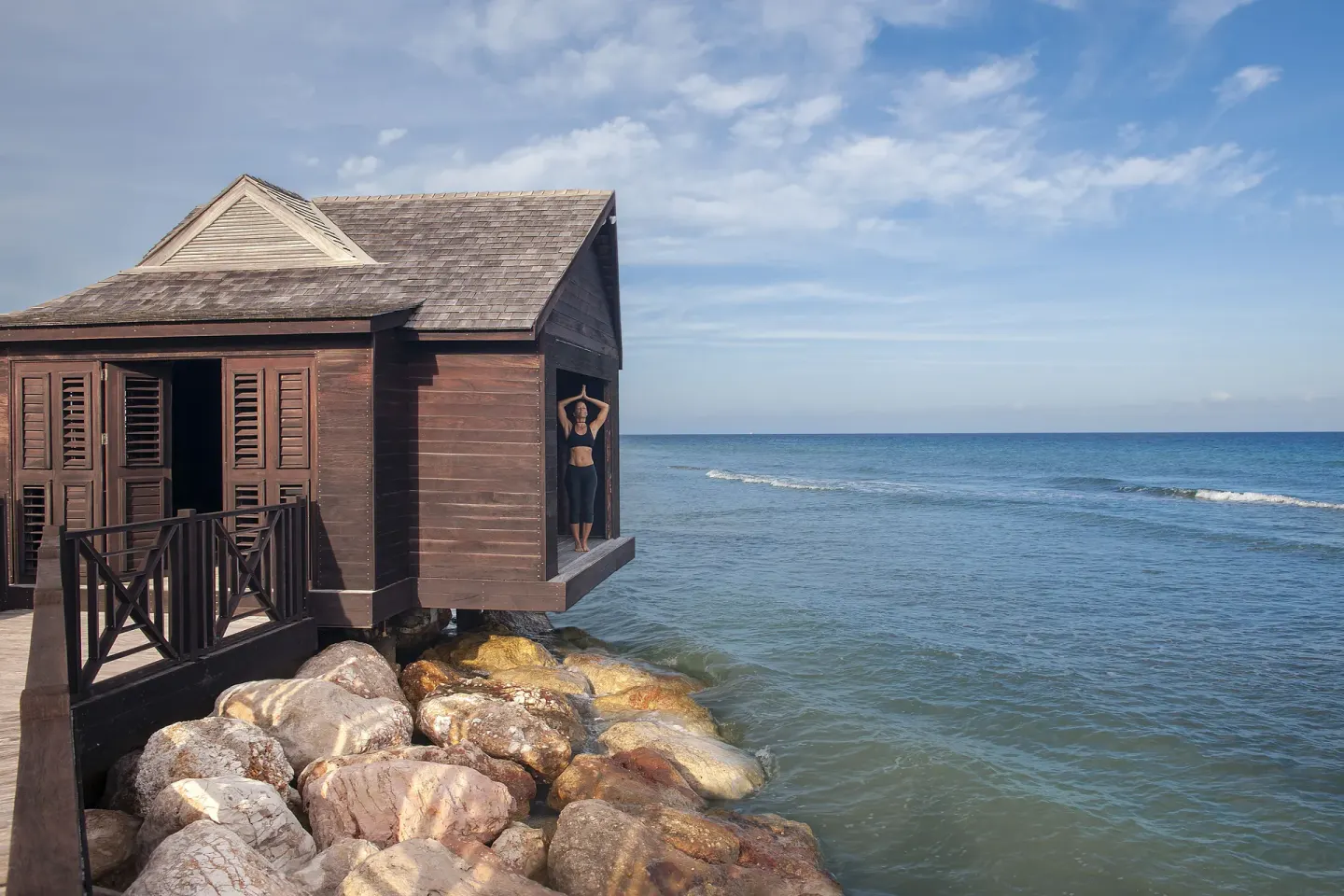 A wooden overwater hut stands beside rocks and the sea at Half Moon.