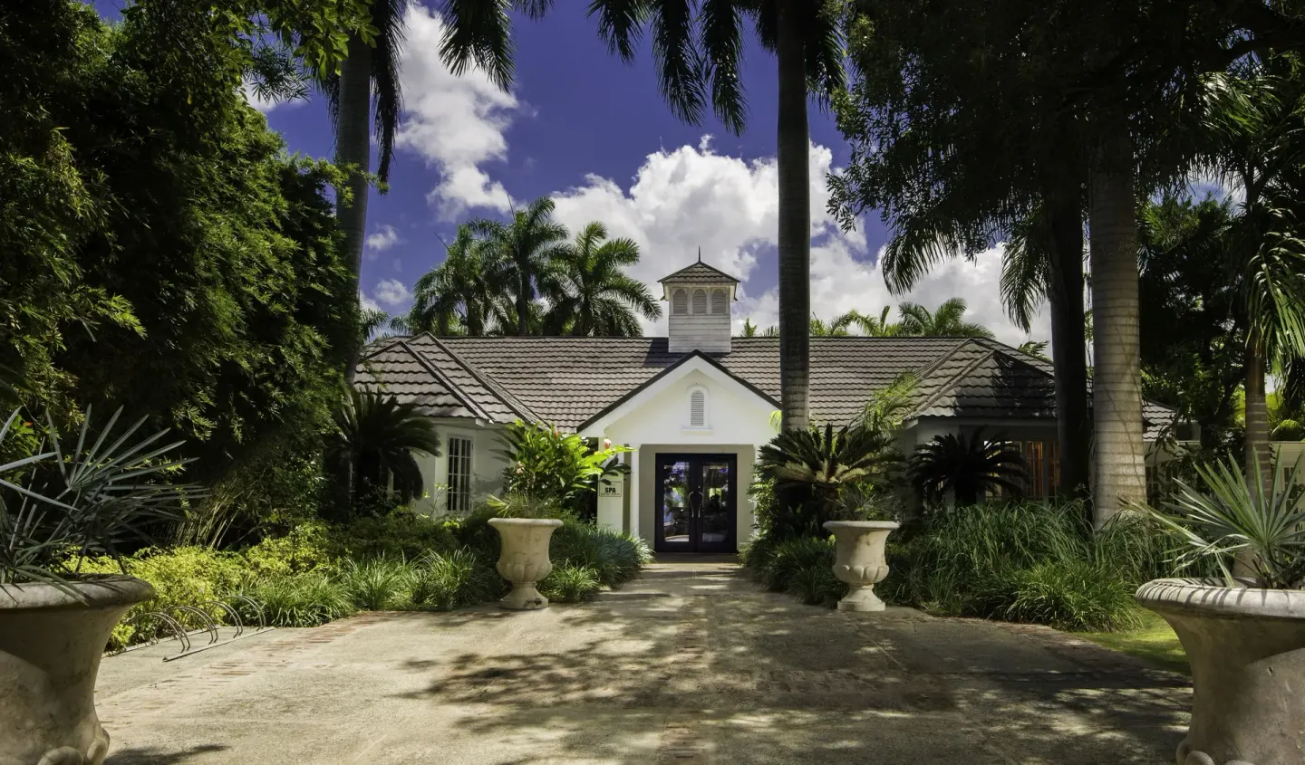 A white spa building is framed by palms and lush gardens at Half Moon.